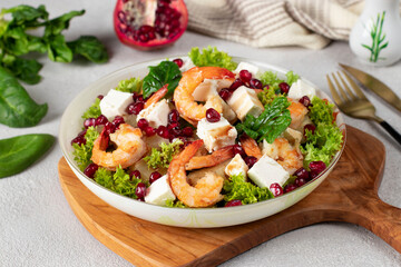 Salad with shrimps, pineapple, feta and pomegranate seeds in a plate on green lettuce leaves, on wooden board