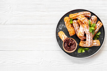Plate with fried churros and chocolate sauce, top view