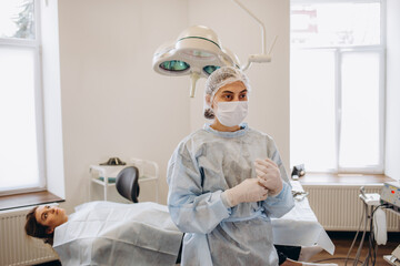 Portrait of Female doctor Surgeon in blue scrubs putting on surgical gloves and Looking at Camera