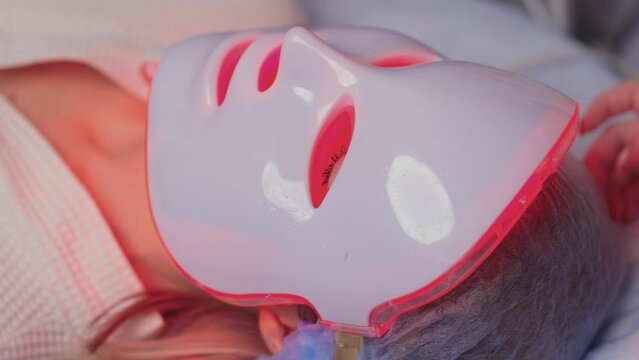 LED light anti-aging mask for facial skin care in a spa slow motion. A woman lies on a couch in a special mask. Modern technologies of beauty and health.