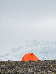 Orange tent on a cliff in glacier. Extreme overnight stay in the mountains. Peace and relaxation in nature. Vertical view.