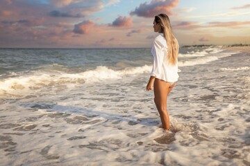 A tanned girl in a blue swimsuit and a light shirt enjoys the summer at the seaside