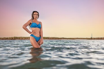 Girl with blond hair in a swimsuit posing against the backdrop of the sunset in the estuary enjoying nature around him