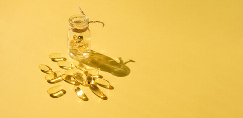 Pills and glass pill bottle on yellow background. Big golden tablets. Omega 3 capsules. Close up,...