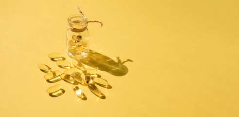 Pills and glass pill bottle on yellow background. Big golden tablets. Omega 3 capsules. Close up, top view. Health care concept. Healthy every day fatty acids nutritional supplement dosage. Flat lay