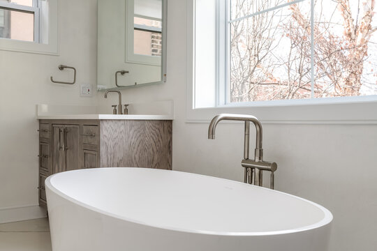 Contemporary Bathroom With Free Standing Soaking Tub. Close Up Of Bathtub With Matte Steel Faucet And Wooden Vanity.