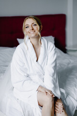 Wedding morning. Beautiful bride in a white robe sitting on the bed in the bedroom.