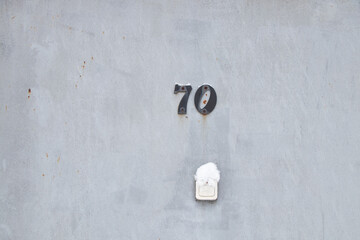 House number 70 on the iron door of the apartment and a bell on the street in the snow in winter in...