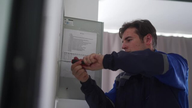 Electrician installs electrical fuse box. Master in uniform tightens screws on electrical panel with screwdriver to fix electricity. Repairman fixing domestic issues.
