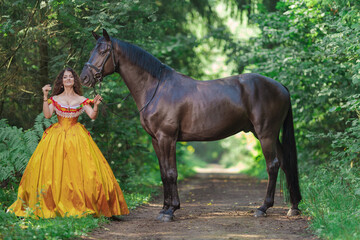 A young woman in a vintage yellow dress walks with a brown horse in a green park on a summer day