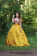A young woman in an ancient medieval yellow orange dress walks in a green park on a sunny summer day