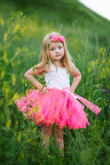 Portrait of a serious child princess in a park. The little girl in a pink dress walks barefoot on...