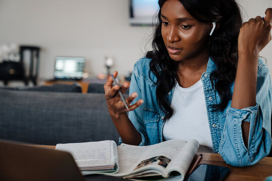 Black young woman in earphones using laptop while doing homework