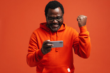Black bearded man making winner gesture and using cellphone