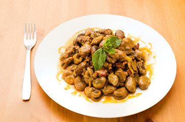 Typical Spanish food, tender broad beans with ham and mint. Horizontal view of food on a white plate.