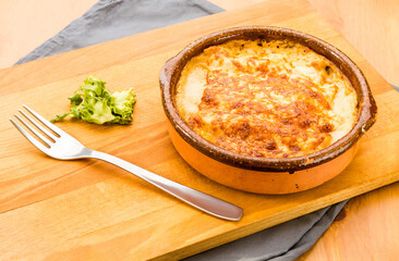 Typical Spanish food, meat lasagna au gratin with cheese. 
Horizontal view of food in a clay pot on a wooden table.