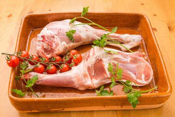 Typical Spanish food, uncooked lamb legs with tomatoes and parsley on a clay pot. Horizontal view of the food.