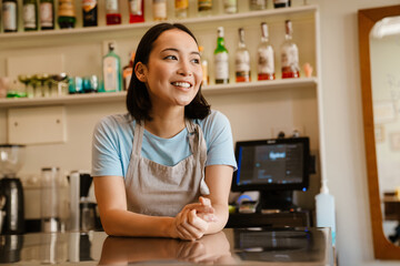 Young asian waitress wearing apron smiling in cafe
