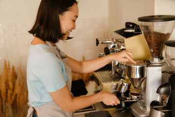 Young asian barista wearing apron smiling while making coffee