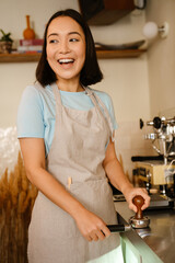 Young asian barista wearing apron laughing while making coffee