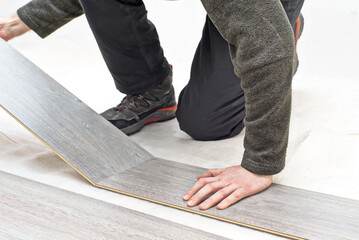 DIY, repair, building and home concept - close up of male hands lying parquet floor board/laminate flooring