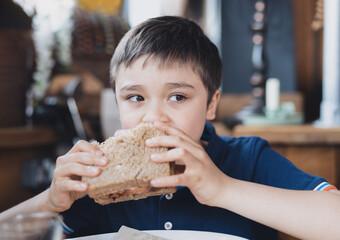 Healthy Kid boy eating homemade bacon sandwich with sliced wholegrain bread. Child having breakfast...