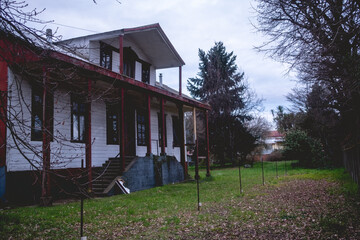 Two story old centuries wood house with stone basement and green garden with grass and big trees in...