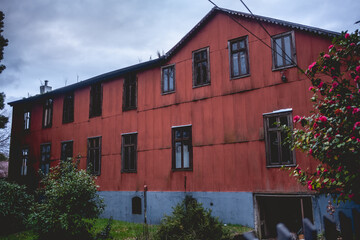 Red two story old centuries wood house with stone basement and green garden with grass and bushes...