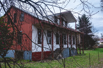 Branches and two story old centuries wood house with stone basement and green garden with grass and...
