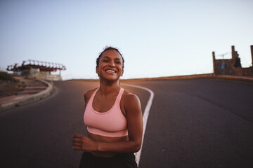 Fototapeta na wymiar Smiling young woman jogging on a road in the morning