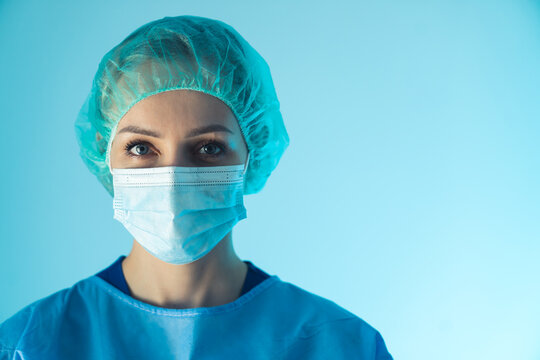 portrait of a young attractive Caucasian female doctor with a surgical mask and blue uniform closeup studio shot indoor blue background copy space healthcare concept . High quality photo