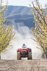 Farmer driving a tractor while spraying insecticide on the field. He wears a chemical protective...