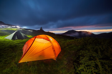 Illuminated orange camping tent under moon