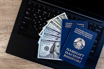 Belarusian passports on the keyboard of a black laptop with cash dollars on a brown wooden table. Travel and remote work concept
