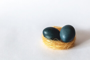 Two matte painted blue Easter eggs in a yellow nest on a gray background. Close-up