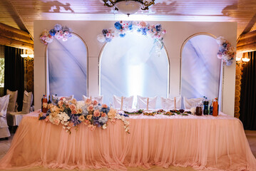 Festive table, arch decorated with composition of blue, white, pink flowers and greenery in the banquet hall. Table newlyweds in the banquet area on wedding party.