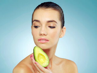 Be nice to your skin and feed it natural oils. Studio shot of a beautiful young woman holding an avocado against a blue background.