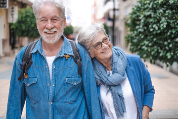 Happy active smiling adult Caucasian senior couple walking in the city holding hands as tourists....