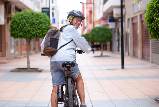 Attractive smiling senior cyclist woman running with electric bicycle in a city street looking at camera. Elderly active grandmother enjoying a healthy lifestyle and free time in retirement