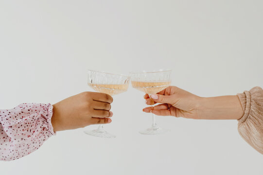 Closeup Of Two Female Hands Clinking Glasses On White Background.