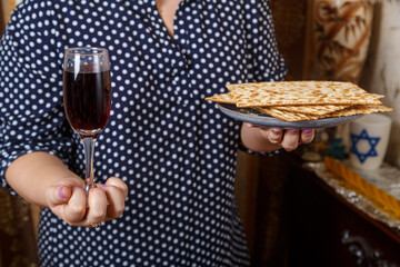 A Jewish woman with a glass of wine and matzah in her hands before the Seder on Pesach.