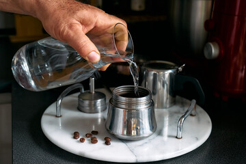 Man preparing classic Italian coffee in the mocha in the kitchen, pouring water into the coffee maker. Coffee brake. Morning habit.
