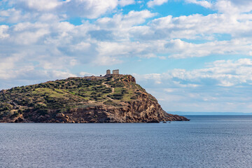 The Temple of Poseidon on a rock rises above the blue sea. Beautiful seascape. Europe, Greece, Cape Sounion, Aegean Sea