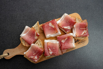 Pieces of bacon thinly sliced on a wooden board. Bread cut for eating.