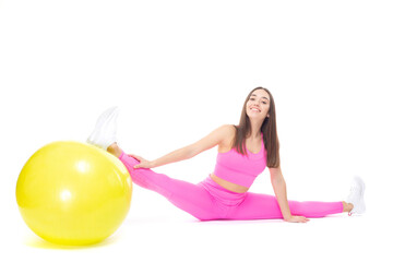 Fototapeta na wymiar A beautiful, athletic, slim, smiling and cheerful woman in a pink tracksuit demonstrates stretching. Sits on a twine supported by a yellow fitball. Pilates. Lifestyle concept with sports and gym