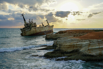 a large rusty shipwreck on a rocky coast against a beautiful sunset background