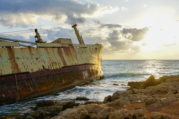 a large rusty shipwreck on a rocky coast against a beautiful sunset background