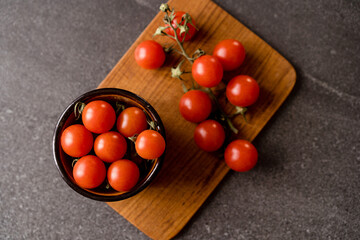 Red cherry tomatoes on a dark stone background and wooden chopping board. 