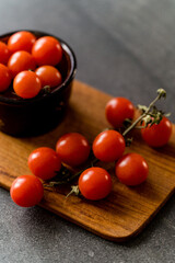 Red cherry tomatoes on a dark stone background and wooden chopping board. 