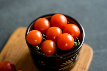 Red cherry tomatoes on a dark stone background and wooden chopping board. 